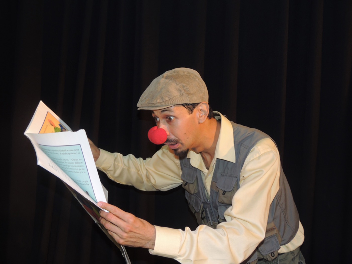 Julio Patricio en personaje, con gorra y nariz roja, leyendo con los ojos muy abiertos de un libro ilustrado grande.