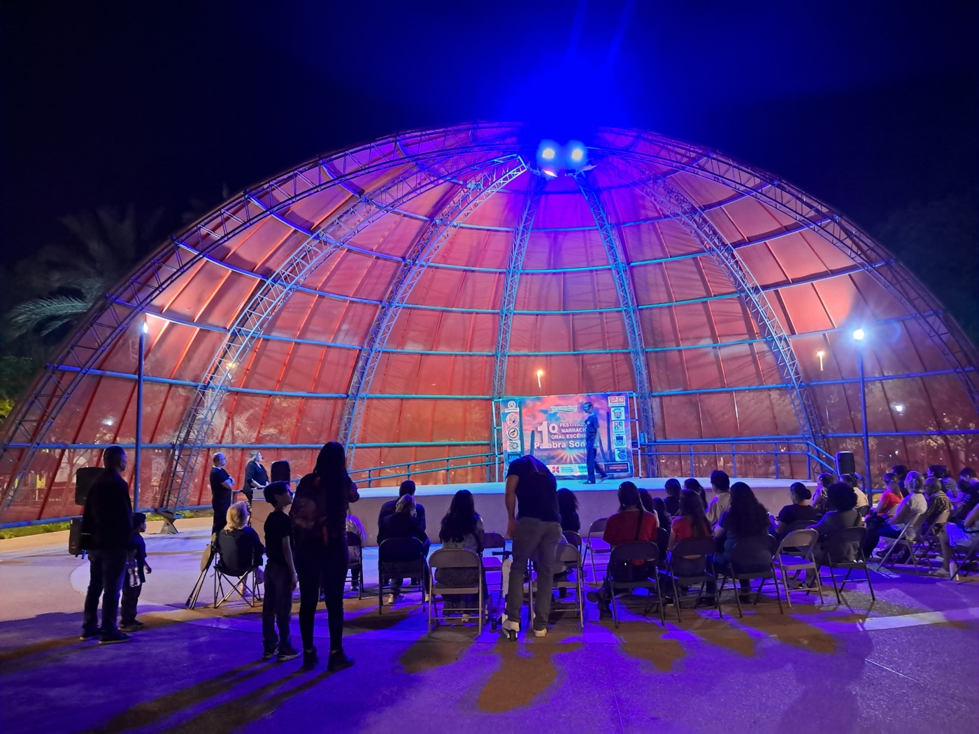 El domo del Parque Madero iluminado de noche, con el público sentado frente al escenario del festival.