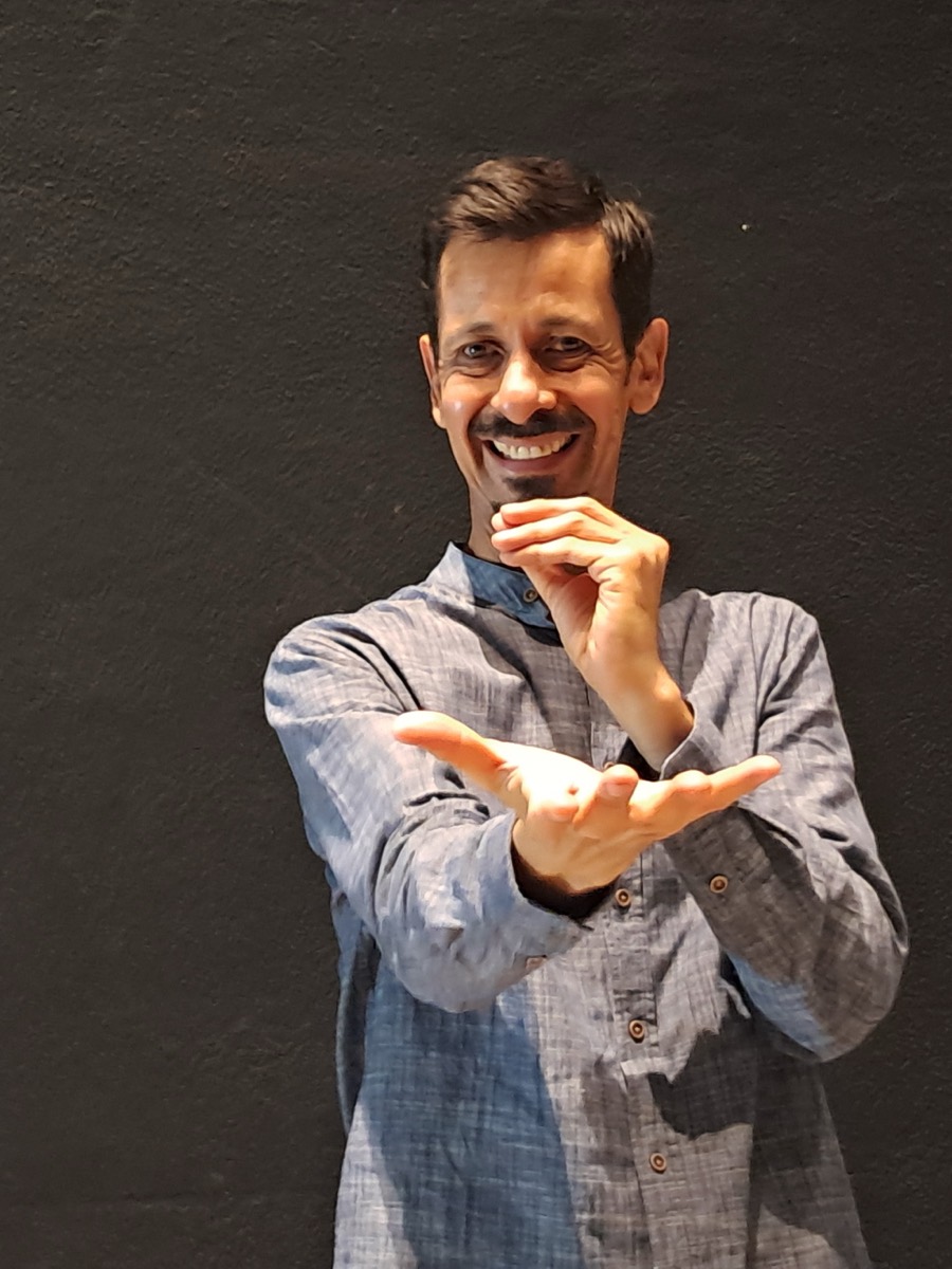 Julio Patricio en el foro, sonriendo, con las manos ahuecadas al frente como si sostuviera algo invisible mientras cuenta.